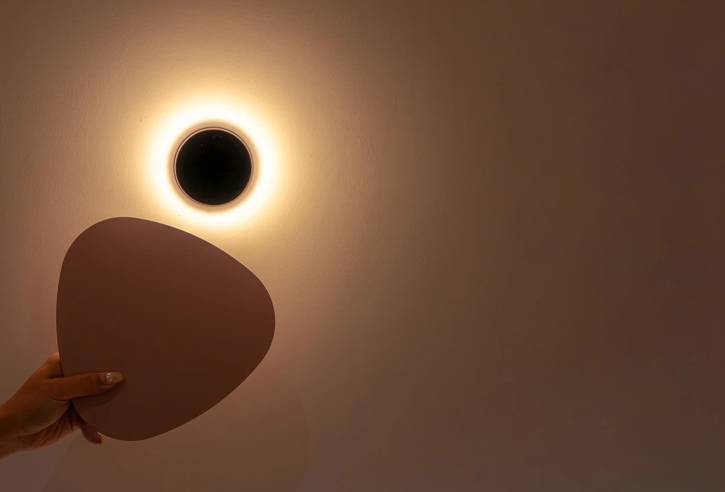 Hand holding decorative wall panel next to circular wall sconce with warm halo light