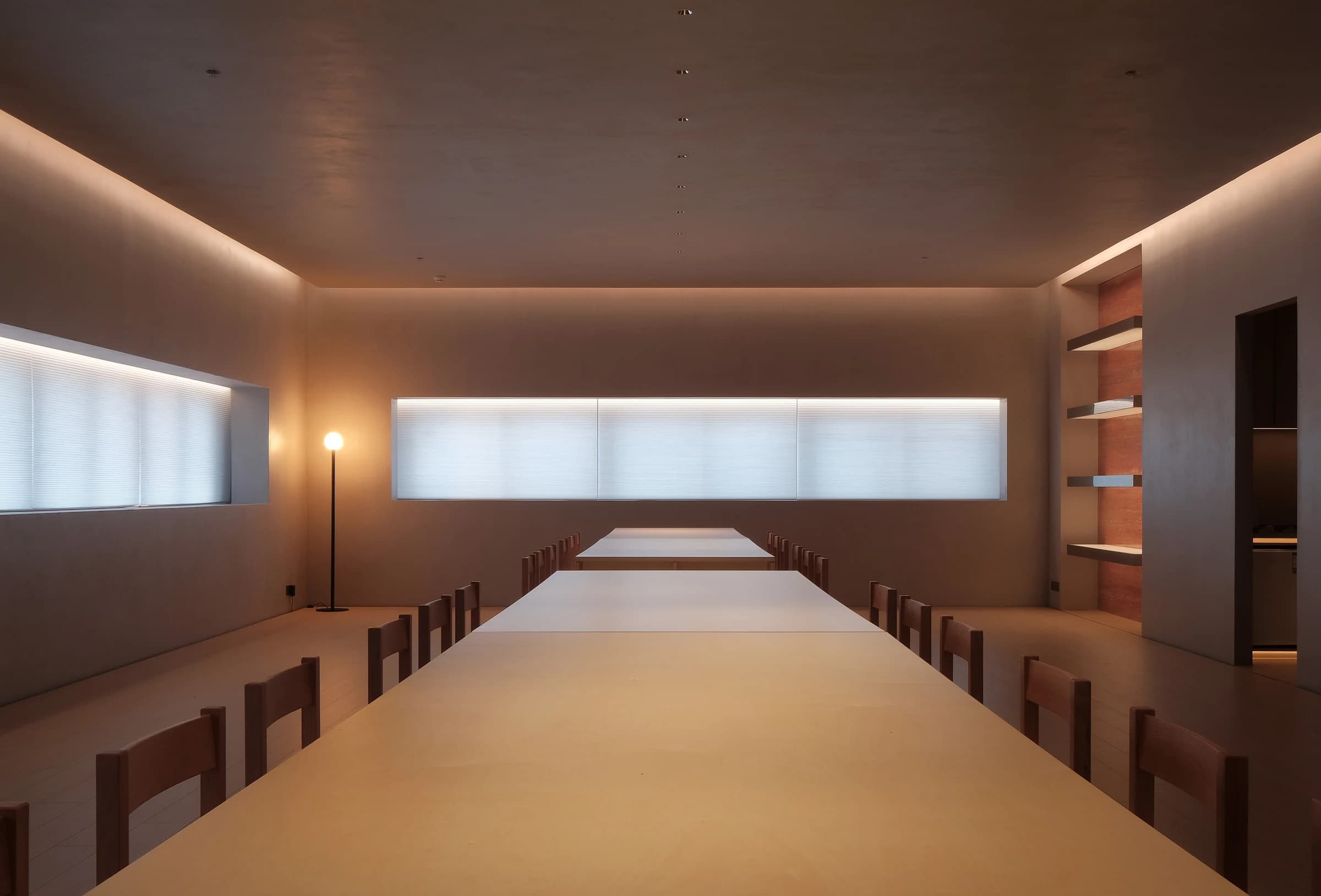 Long dining hall with recessed ceiling spotlights, cove lighting and warm material palette