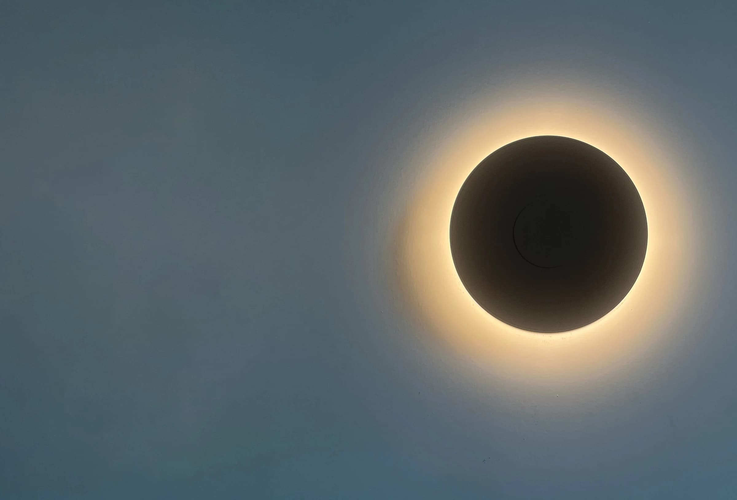 Eclipse-shaped wall sconce casting warm halo glow on blue-grey textured wall