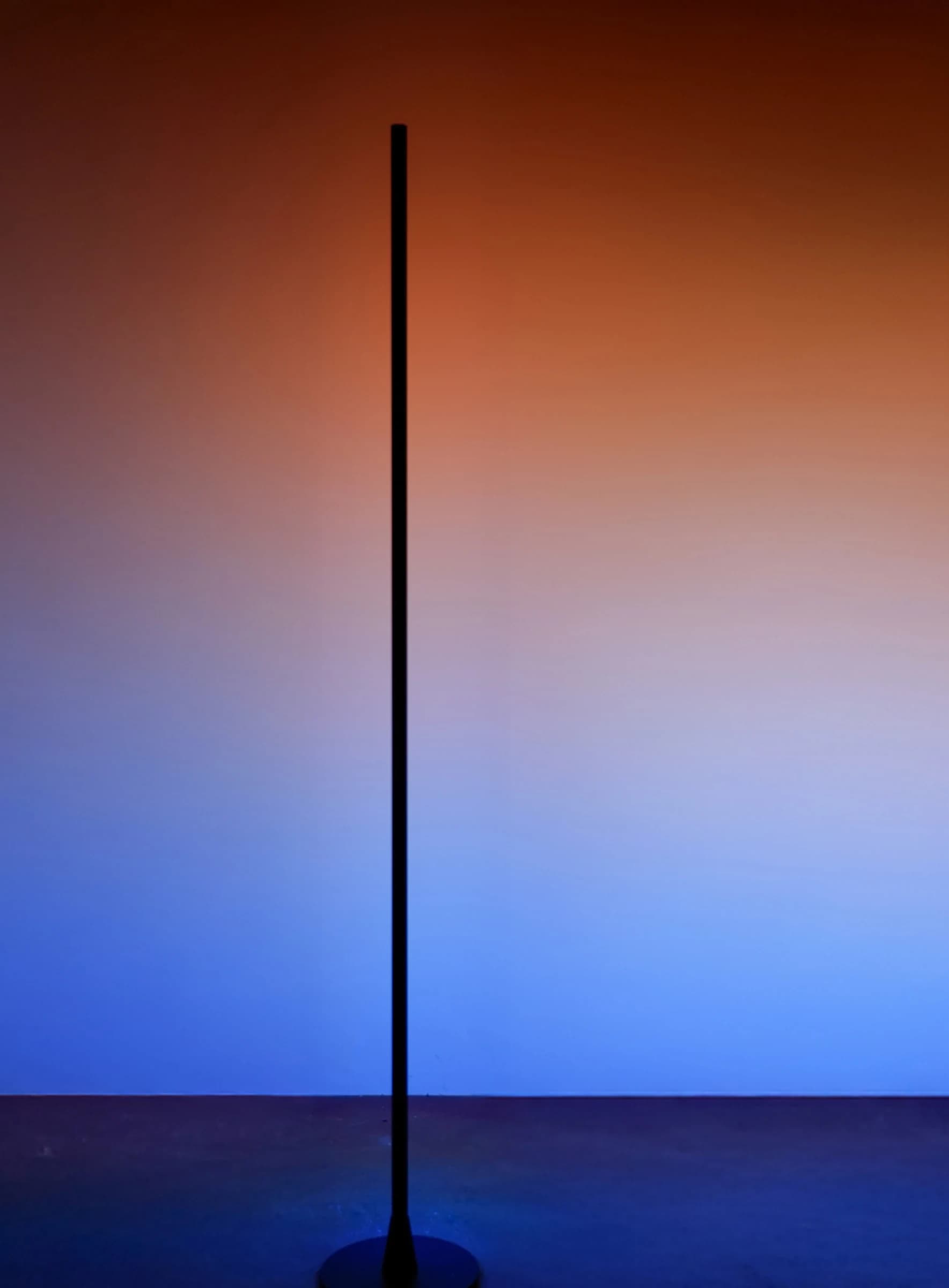 Silhouette of slender floor lamp against warm sunset-to-blue gradient backdrop