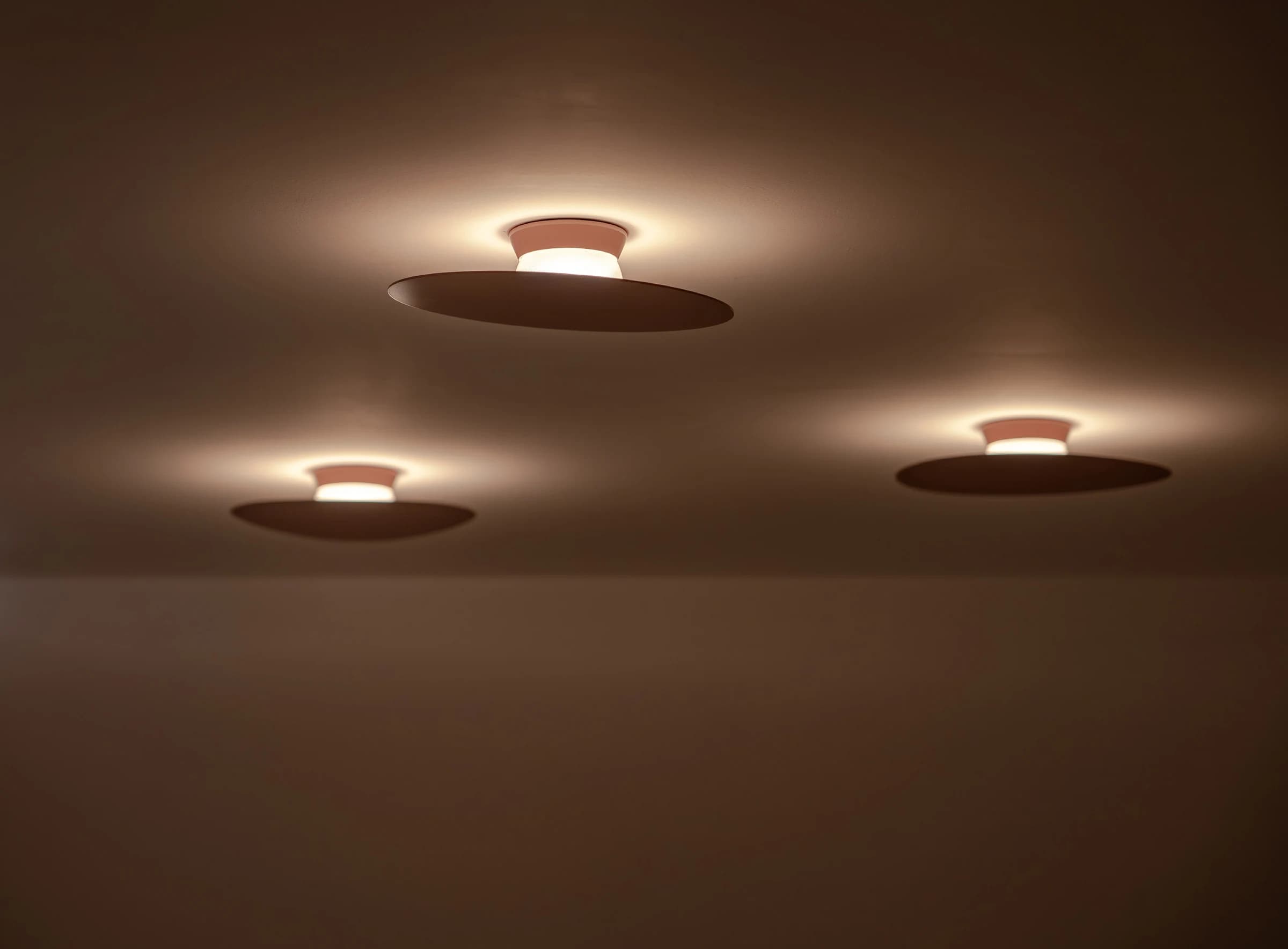 Three ceiling-mounted disc fixtures creating warm upward light pools on plastered ceiling